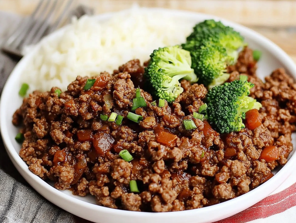 A plate of ground beef broccoli served with fluffy white rice, featuring tender beef, fresh broccoli florets, and garnished with green onions.