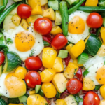 A colorful vegetable and egg breakfast skillet with cherry tomatoes, zucchini, yellow bell peppers, green beans, and sunny-side-up eggs.